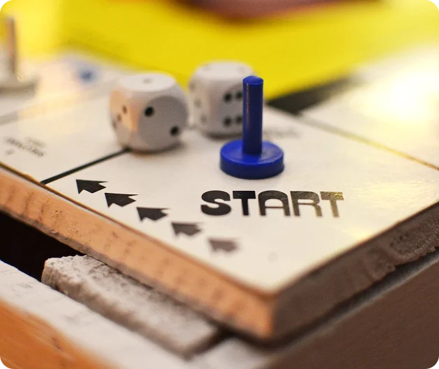 Een blauw speelstuk op het startvak van een bordspel met dobbelstenen op de achtergrond