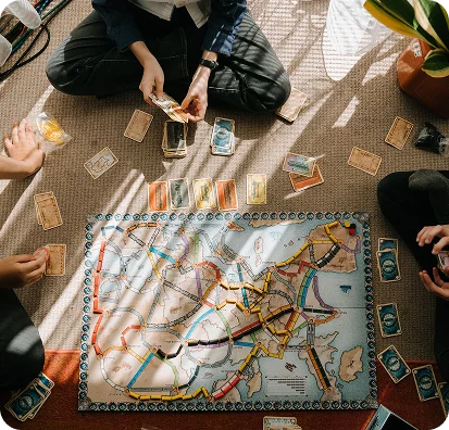 Het gezin zit op de vloer en speelt het bordspel Ticket to Ride met een kaart van Europa en treinen