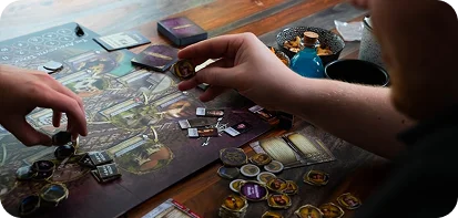 Close-up van spelers die interactie hebben met kaarten, tokens en spelstukken tijdens een strategische tabletop bordspel sessie.